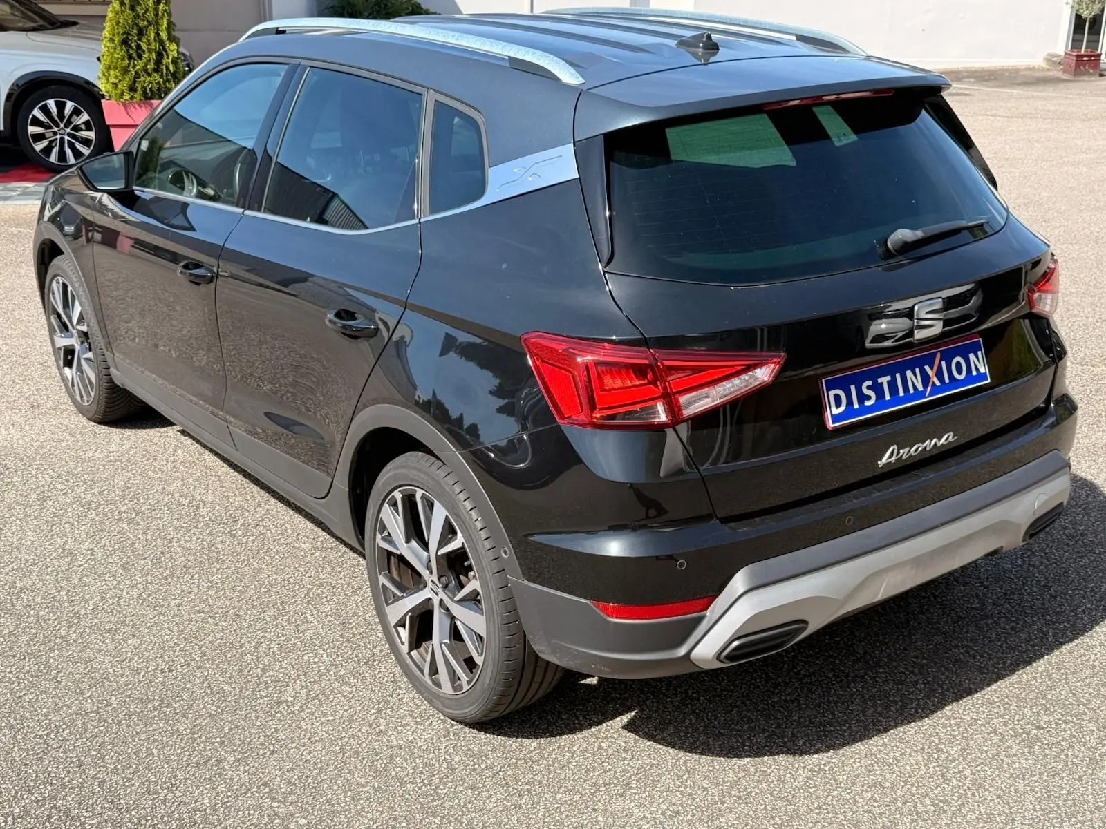 Vue 3/4 arrière droite d'une SEAT Arona noire avec toit et barres de toit argentés, jantes alliage et feux LED distinctifs.