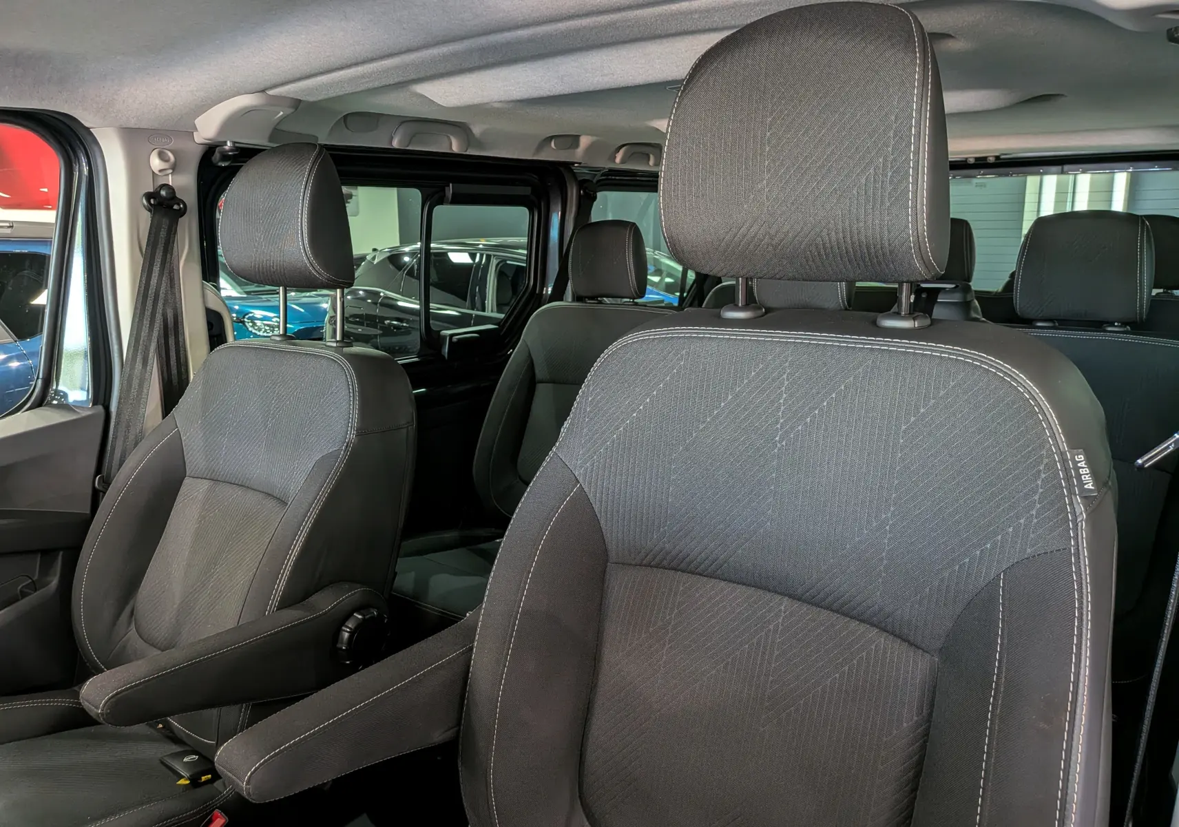 Vue intérieure rapprochée des sièges avant en tissu gris foncé du Nissan Primastar Combi L1H1 2025.