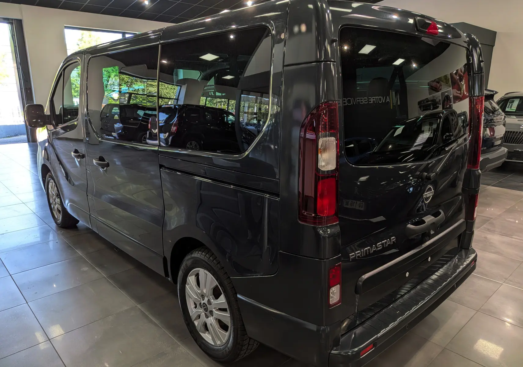 Vue 3/4 arrière droite du Nissan Primastar Combi gris comète, avec vitres teintées et feux arrière verticaux allongés.