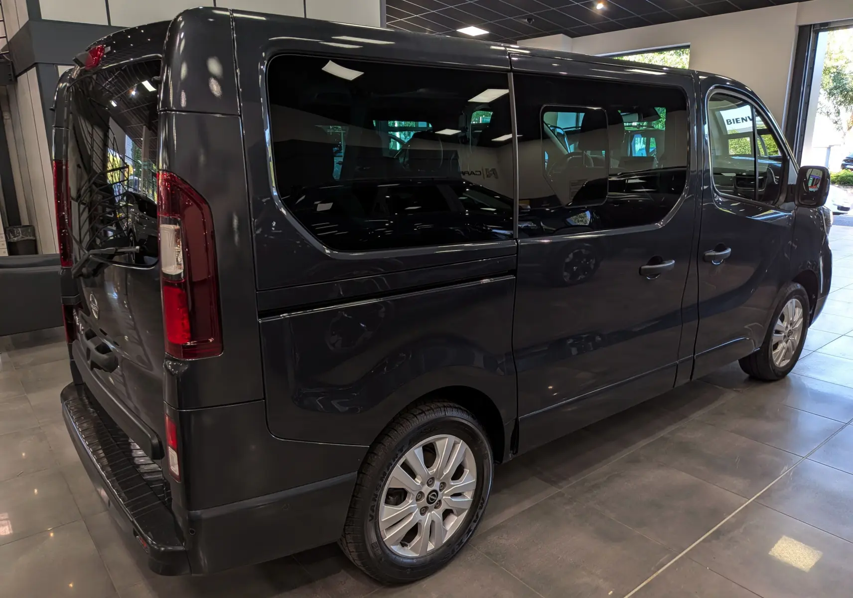 Vue 3/4 arrière droit du Nissan Primastar Combi gris comète 2025, avec vitres teintées et jantes alliage.