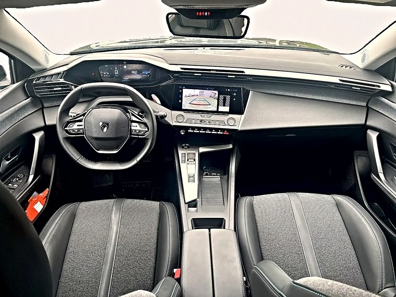 Vue intérieure avant de la Peugeot 308 2025 noire, montrant volant multifonction, écran tactile et sièges tissu gris tremezzo.