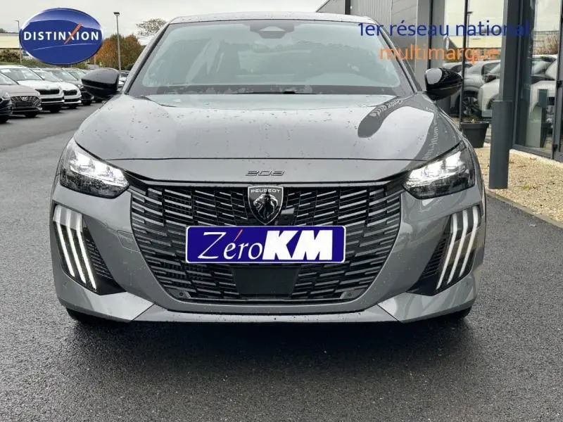 Vue frontale d'une Peugeot 208 grise 2025 avec feux diurnes à LED en forme de griffes et calandre noire distinctive.