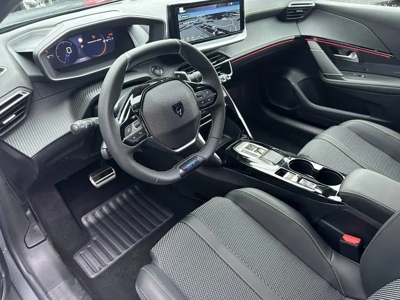 Intérieur noir de la Peugeot 208 Hybrid 2025 vu côté conducteur, avec tableau de bord numérique et écran tactile central.