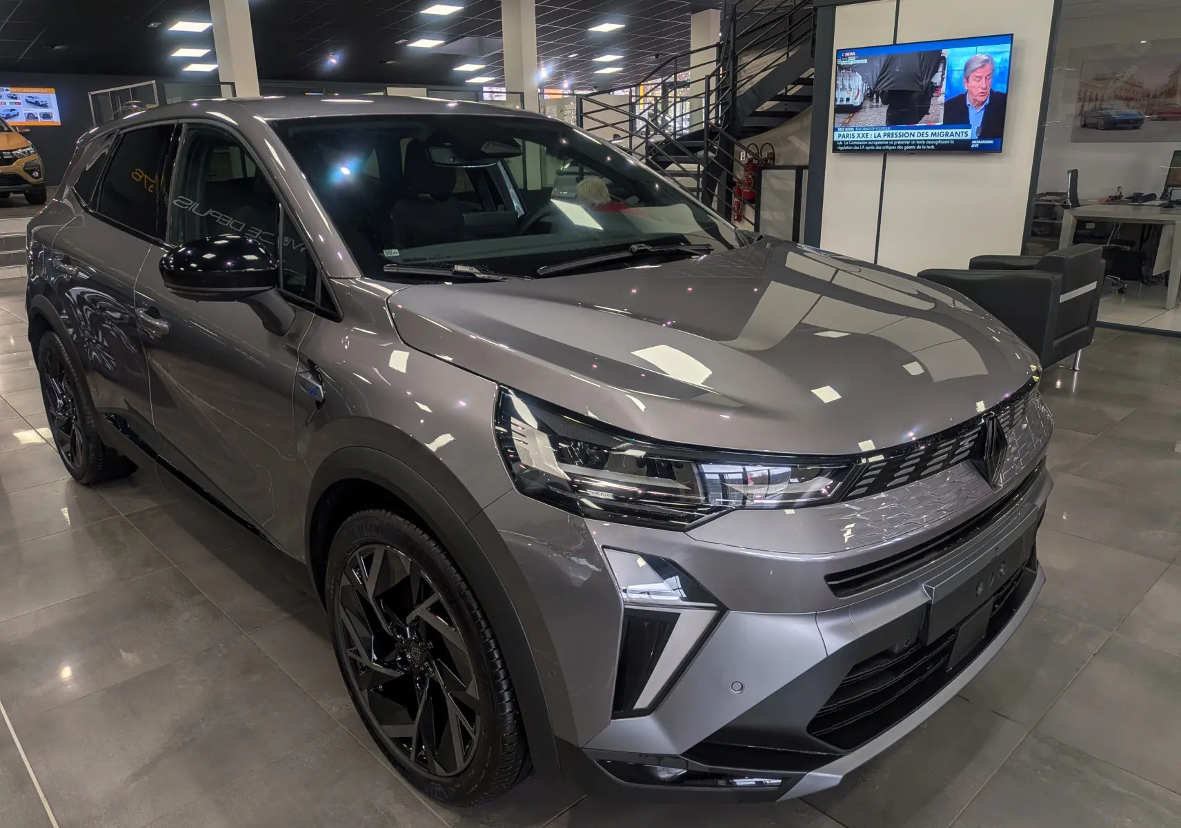 Renault Symbioz gris Cassiopé en 3/4 avant droit, mettant en valeur ses optiques LED et jantes noires brillantes.