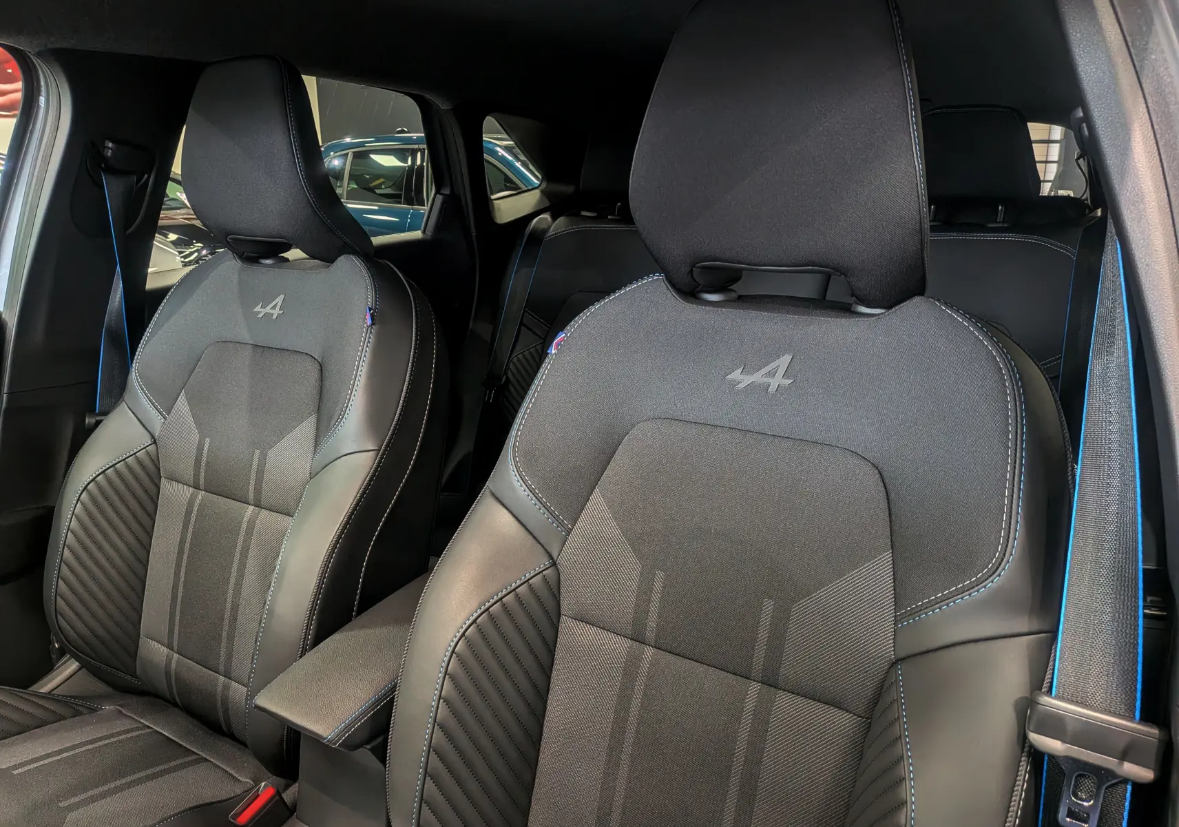 Gros plan sur les sièges avant noirs avec surpiqûres bleues et logo Alpine du Renault Symbioz gris Cassiopé.
