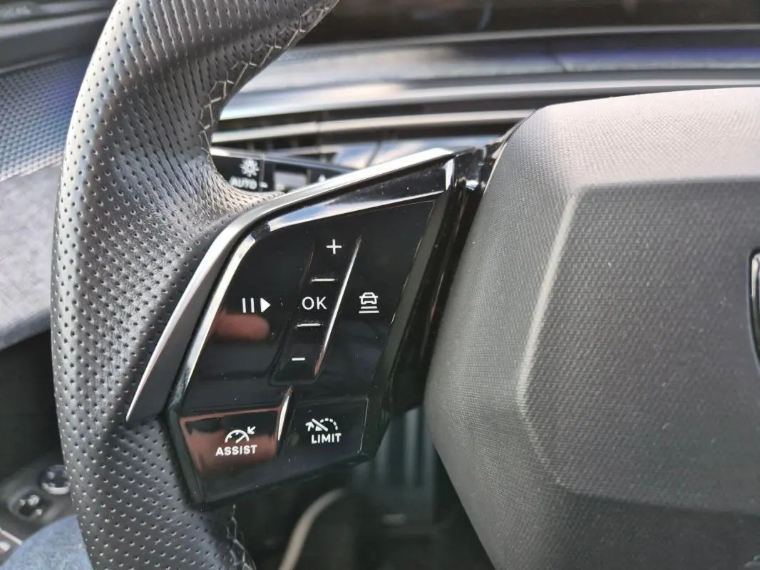Gros plan sur les commandes du volant perforé du Peugeot 3008 Hybrid 136 e-DCS6 GT, finition noire brillante.