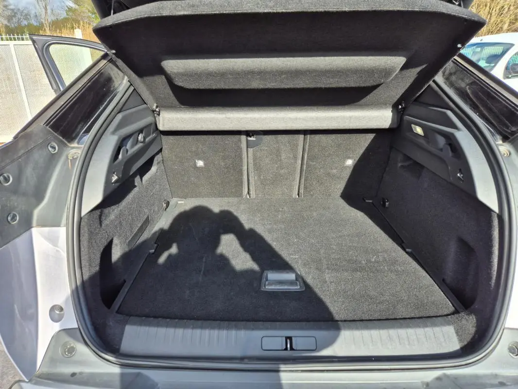 Coffre ouvert vu de l'arrière d'un Peugeot 3008 Hybrid gris clair, montrant un espace de chargement propre et spacieux.