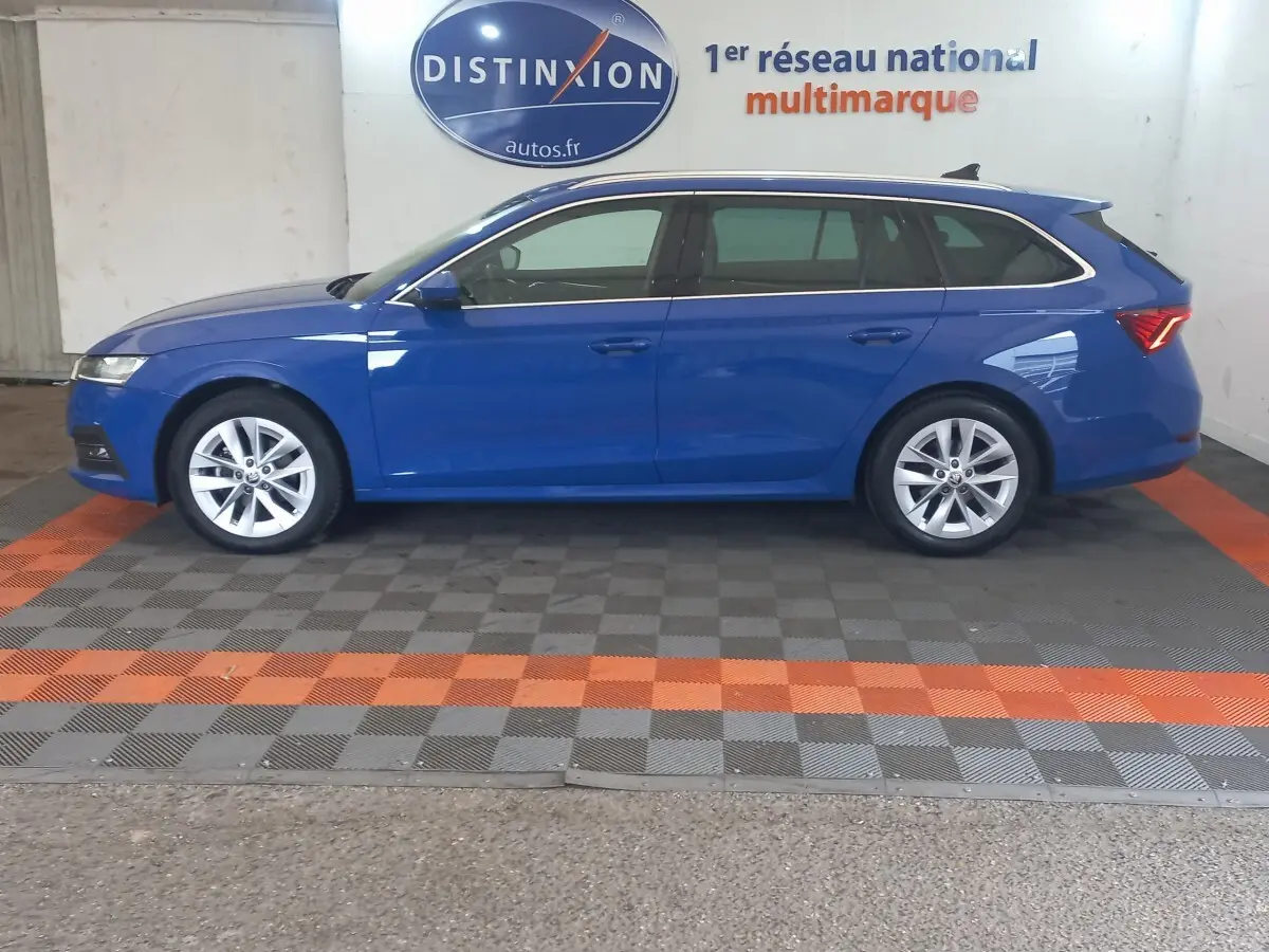 Vue de profil droit d'une Skoda Octavia break bleu 2022 stationnée en intérieur avec jantes argentées et vitres teintées.