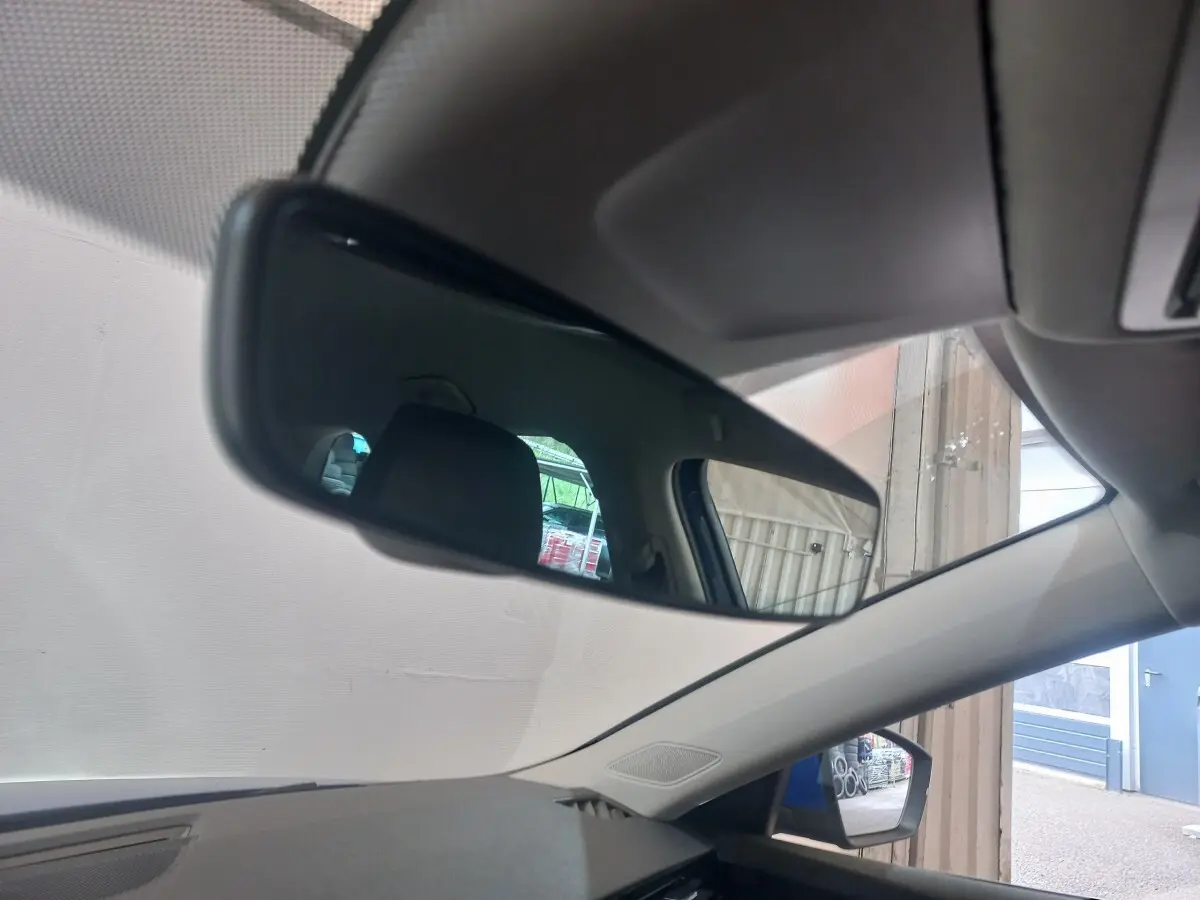 Vue intérieure du rétroviseur central d'une Skoda Octavia 1.5 TSI bleu, avec reflet du siège arrière et fenêtre latérale.
