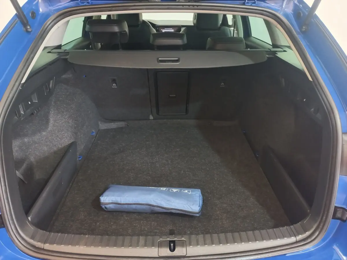 Coffre ouvert vu de l'arrière d'une Skoda Octavia bleu 2022, avec tapis gris et trousse bleue posée au centre.