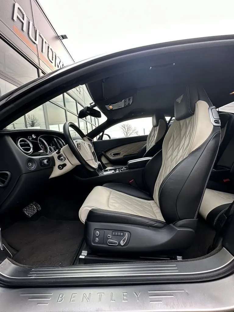 Intérieur de la Bentley Continental GT 4.0 V8 Mulliner 2013 vue côté conducteur, sièges cuir noir et beige avec logo brodé.