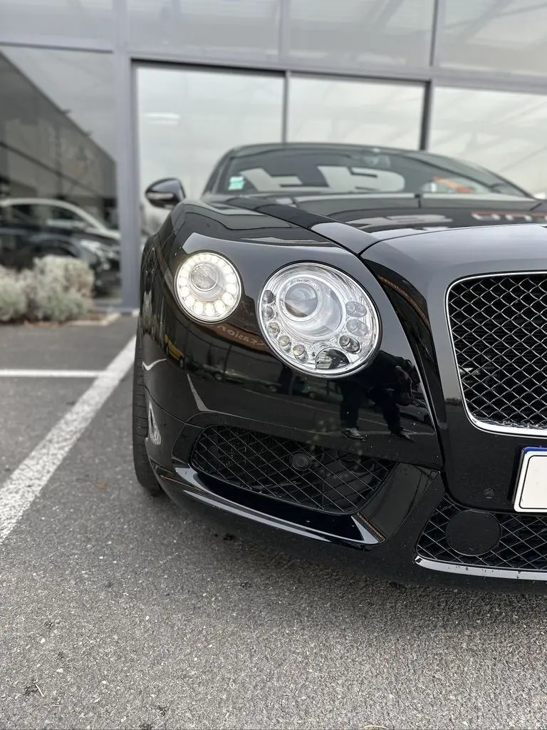 Vue rapprochée 3/4 avant gauche du Bentley Continental GT Mulliner noire, mettant en valeur ses phares ronds distinctifs.
