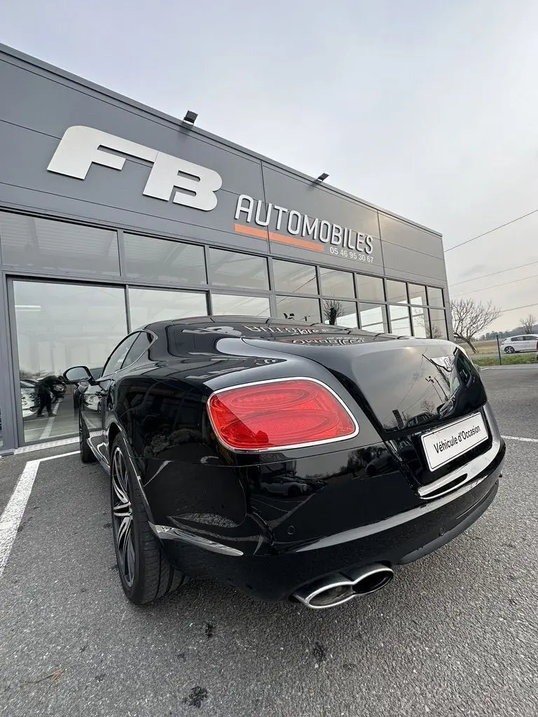 Vue 3/4 arrière droite d'une Bentley Continental GT Mulliner noire de 2013, avec feux arrière rouges et double sortie d'échappement chromée.