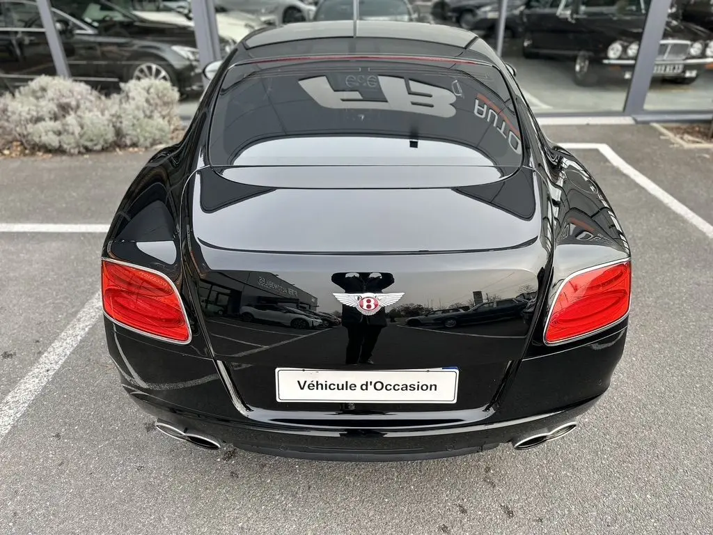 Vue arrière d'une Bentley Continental GT 4.0 V8 Mulliner noire de 2013 avec feux rouges et double sortie d'échappement chromée.