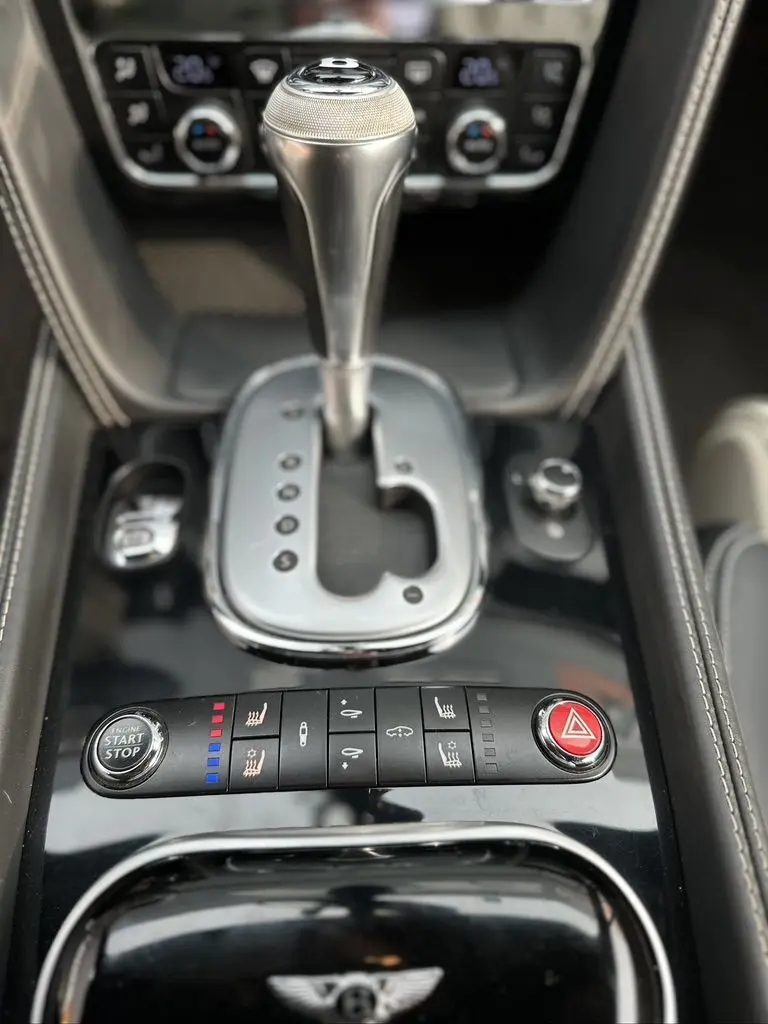 Gros plan sur la console centrale noire de la Bentley Continental GT 2013, mettant en valeur le levier de vitesse automatique et les commandes chauffantes.