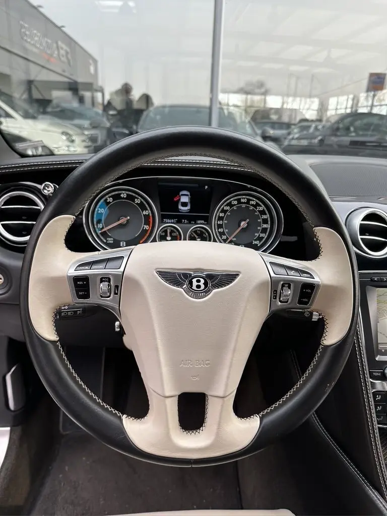 Vue intérieure centrée sur le volant bicolore noir et beige de la Bentley Continental GT Mulliner 2013 avec tableau de bord visible.