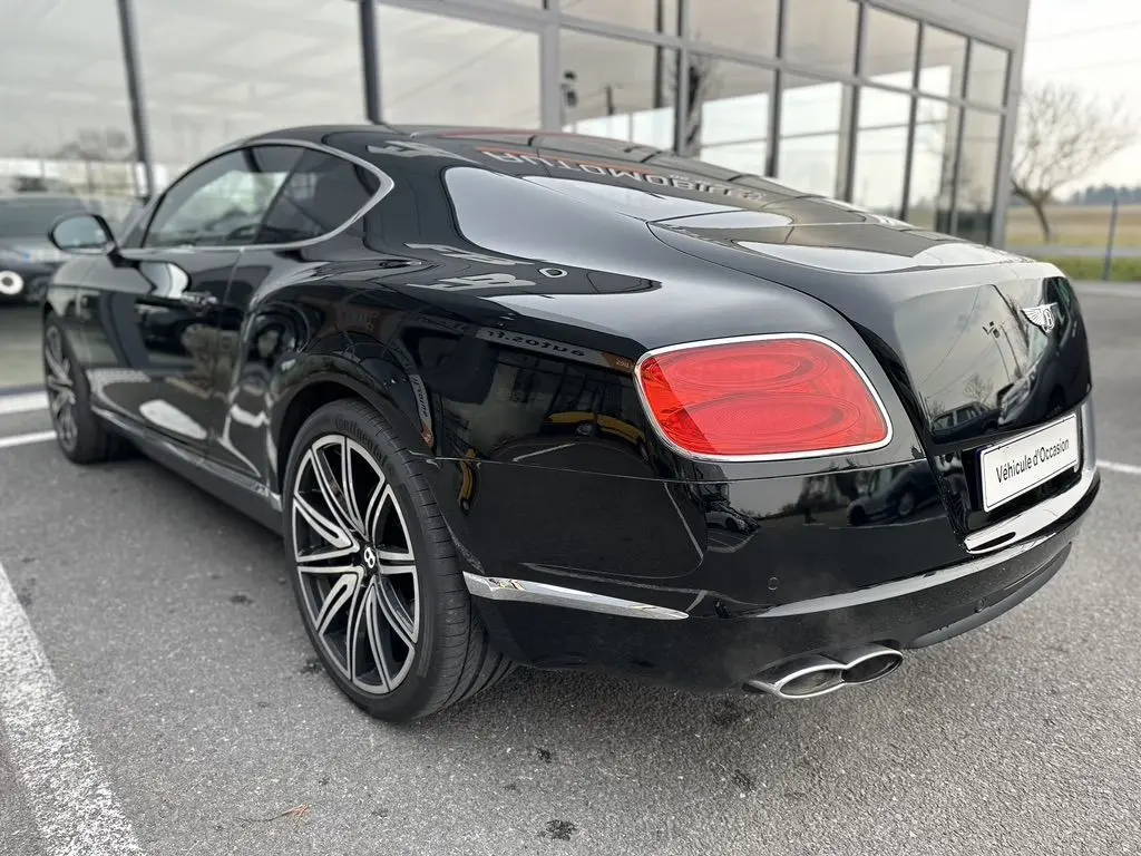 Vue 3/4 arrière droite d'une Bentley Continental GT Mulliner noire de 2013 avec jantes distinctives et double sortie d'échappement.