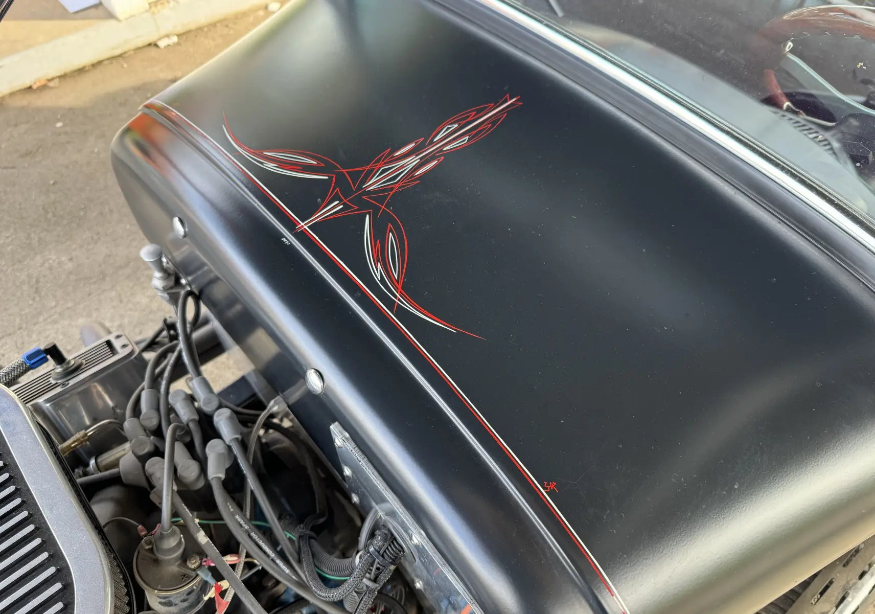 Gros plan sur le capot noir mat du Ford T Hot Rod 1923 avec motifs rouges peints à la main, moteur V8 visible dessous.