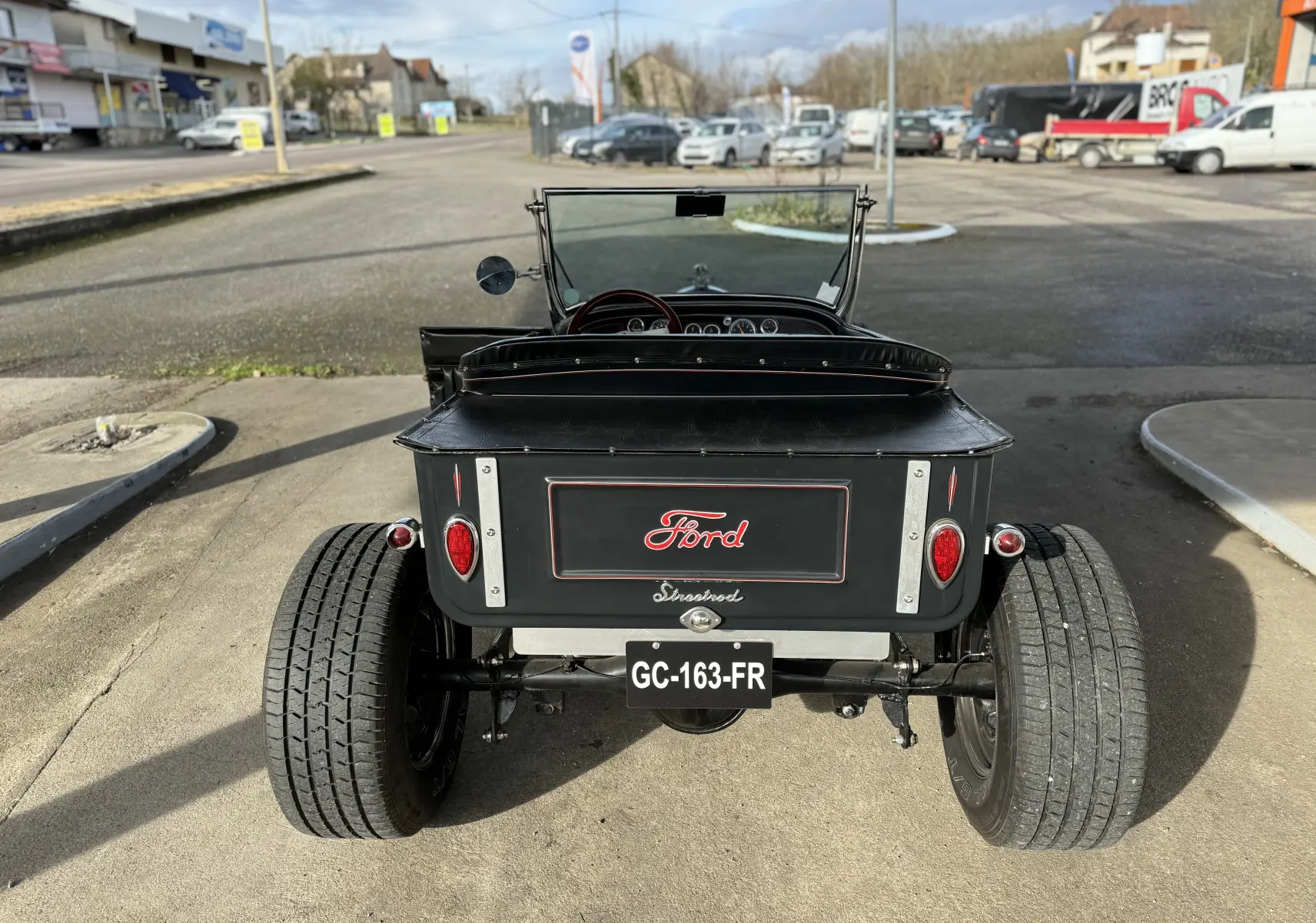 Vue arrière d'une Ford T Hot Rod V8 noire décapotable, avec larges pneus et logo Ford rouge sur le coffre.