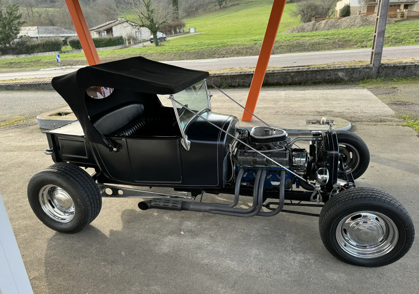 Ford T Hot Rod V8 noir vue de profil côté gauche, capote noire relevée et moteur V8 apparent avec échappements latéraux.