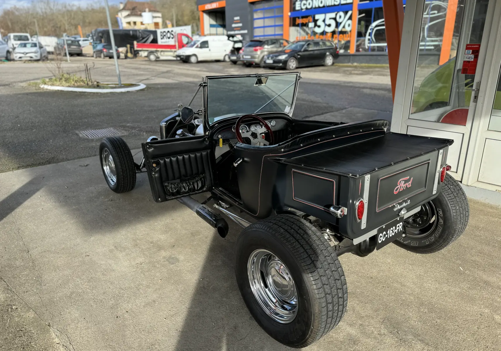 Ford T Hot Rod V8 noir vue 3/4 arrière droit, capote manuelle ouverte et intérieur cuir visible.