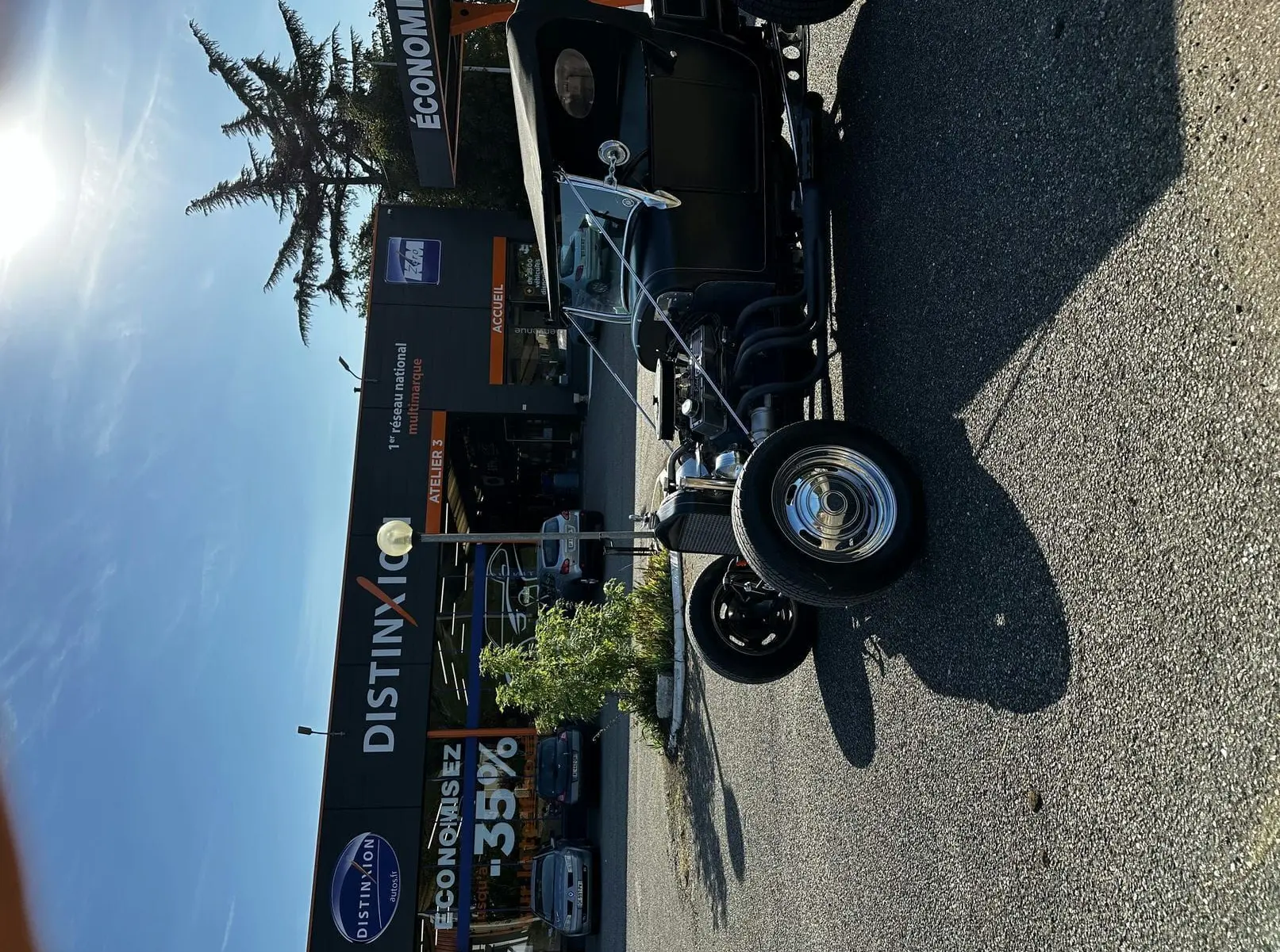 Ford T Hot Rod V8 noir vue 3/4 avant droit, capote relevée et jantes chromées brillantes sur parking.