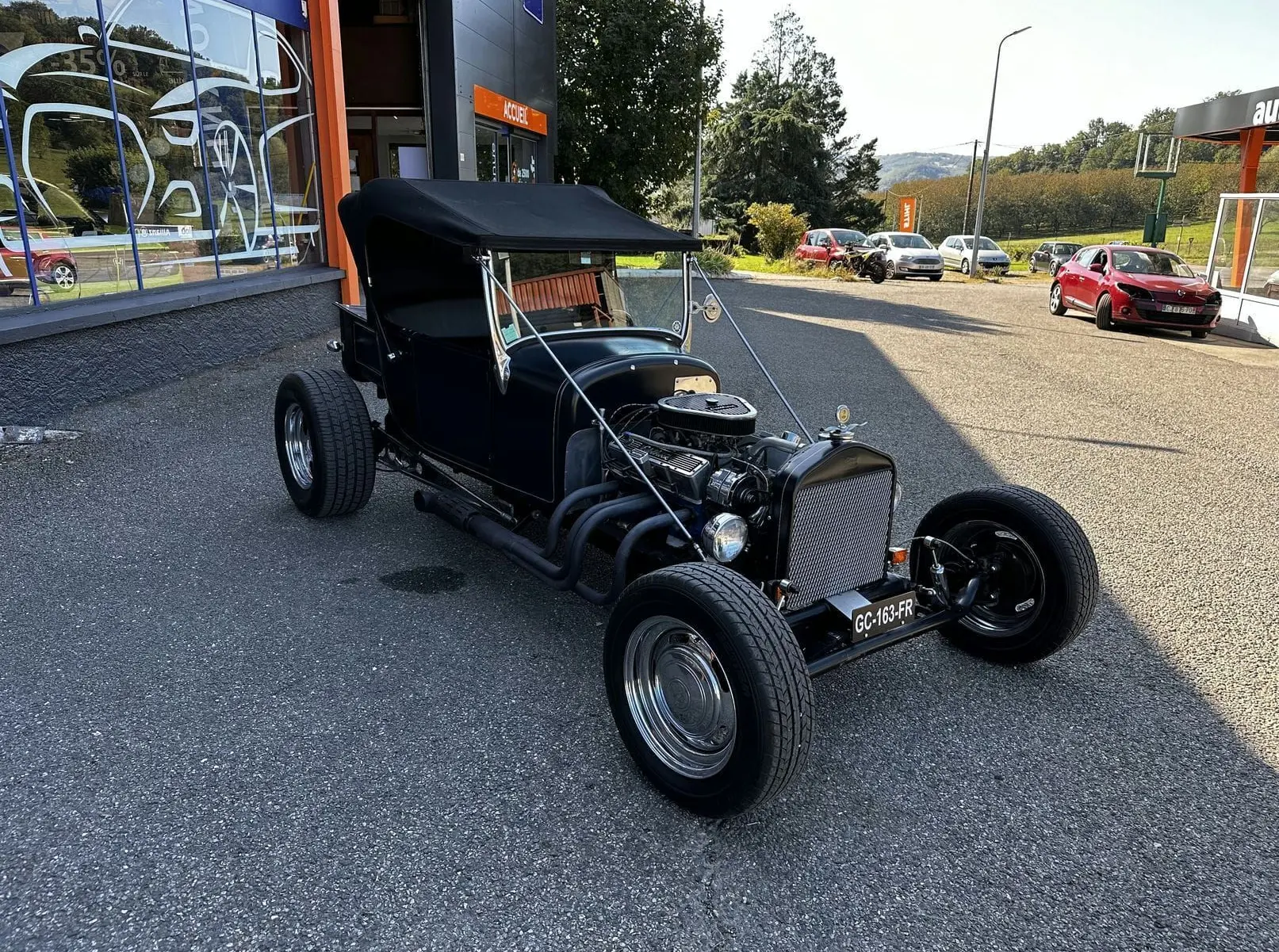 Ford T Hot Rod V8 noir vue 3/4 avant droit, capote relevée et moteur V8 apparent sur parking extérieur.