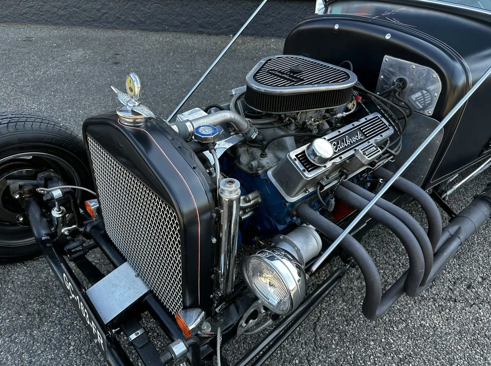 Vue avant droite du Ford T Hot Rod noir avec moteur V8 apparent et échappements latéraux mat.