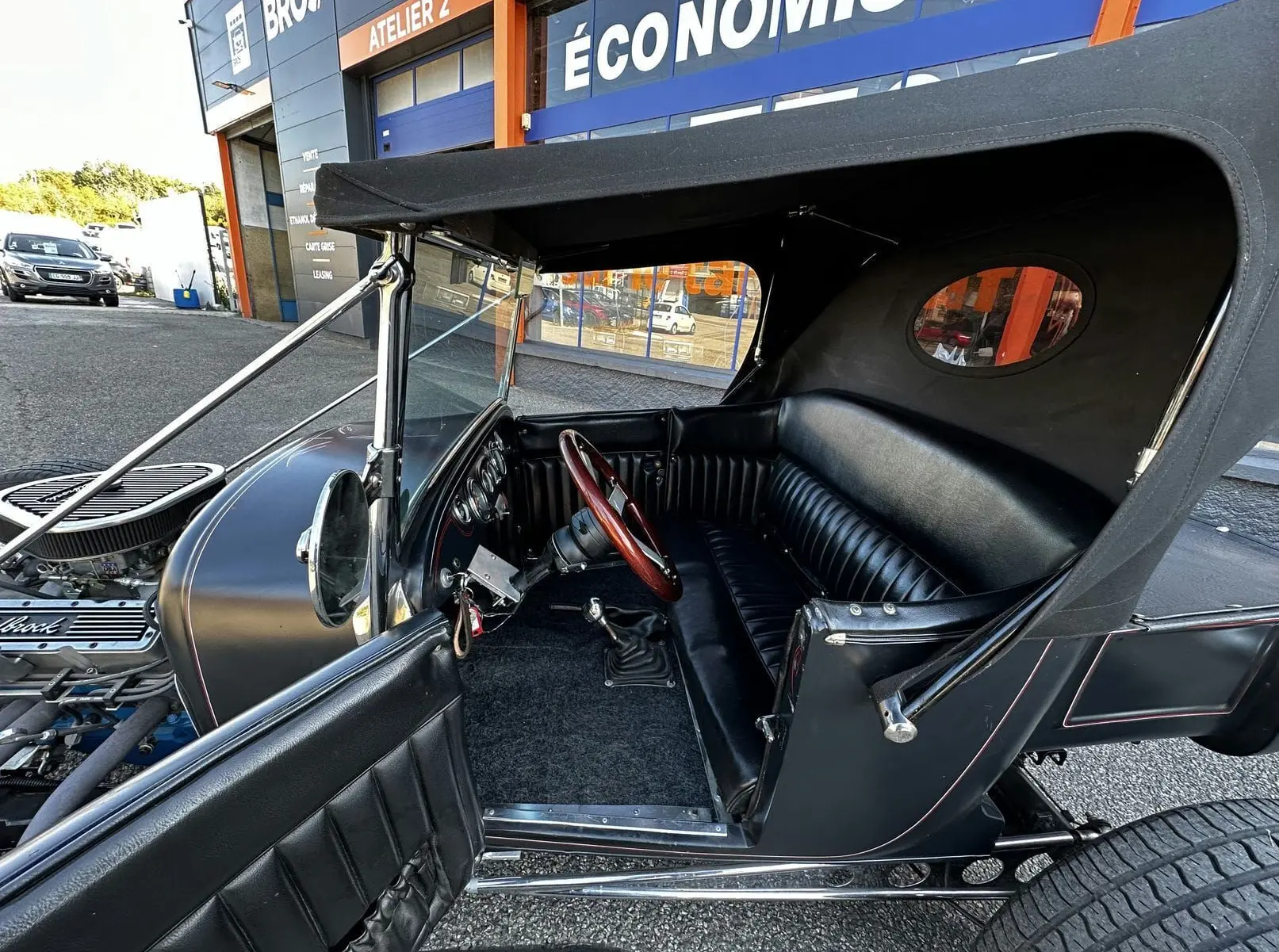 Vue côté gauche intérieur du Ford T Hot Rod V8 noir, banquette cuir et volant bois visibles sous capote décapotable.