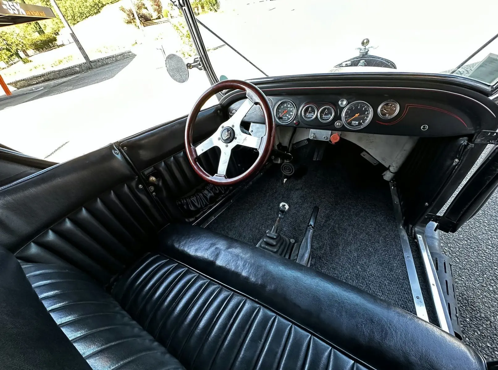 Vue intérieure côté conducteur de la Ford T Hot Rod 1923 noire, volant bois GT et tableau de bord avec compteurs ronds.