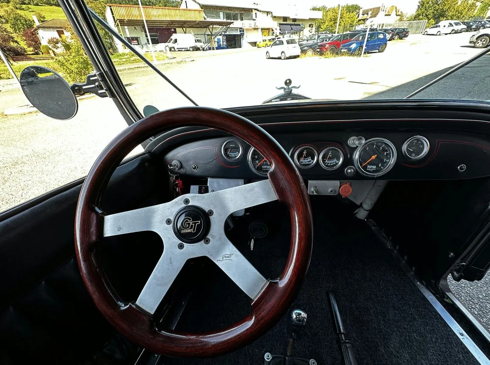 Vue intérieure du volant bois GT et tableau de bord noir du Ford T Hot Rod V8 de 1923 avec compteurs ronds visibles.