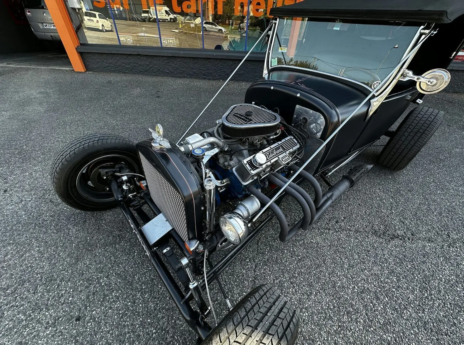Vue 3/4 avant droite d'une Ford T Hot Rod noire avec moteur V8 visible et échappements latéraux exposés.