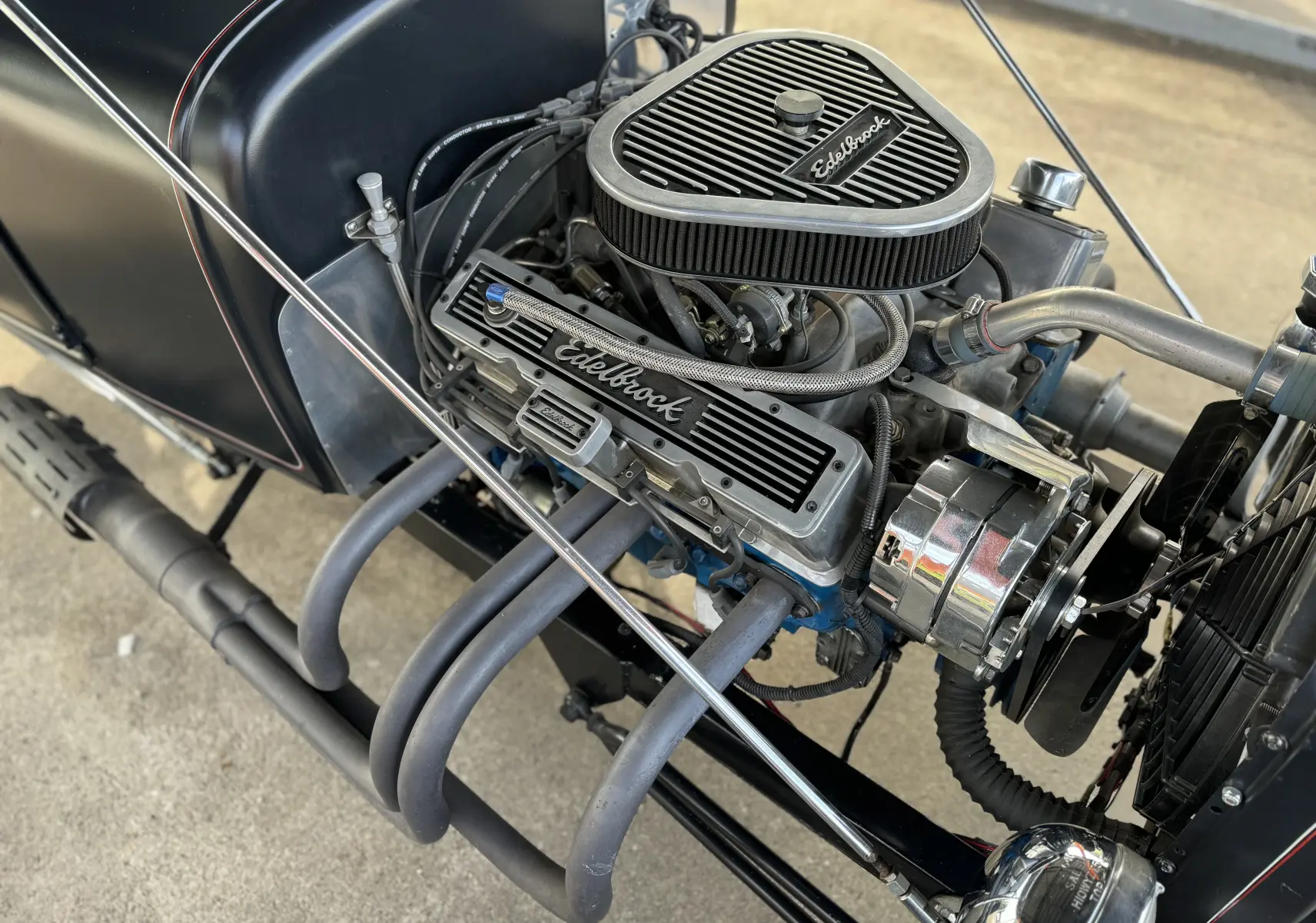 Gros plan sur le moteur V8 Edelbrock du Ford T Hot Rod noir de 1923, avec ses tuyaux d'échappement et détails chromés visibles.