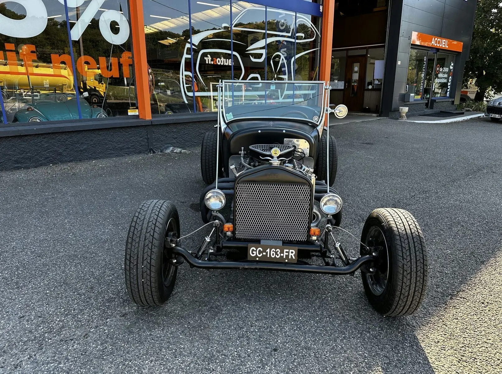 Ford T Hot Rod V8 noir vue de face, capot ouvert dévoilant le moteur et calandre en métal ajouré.