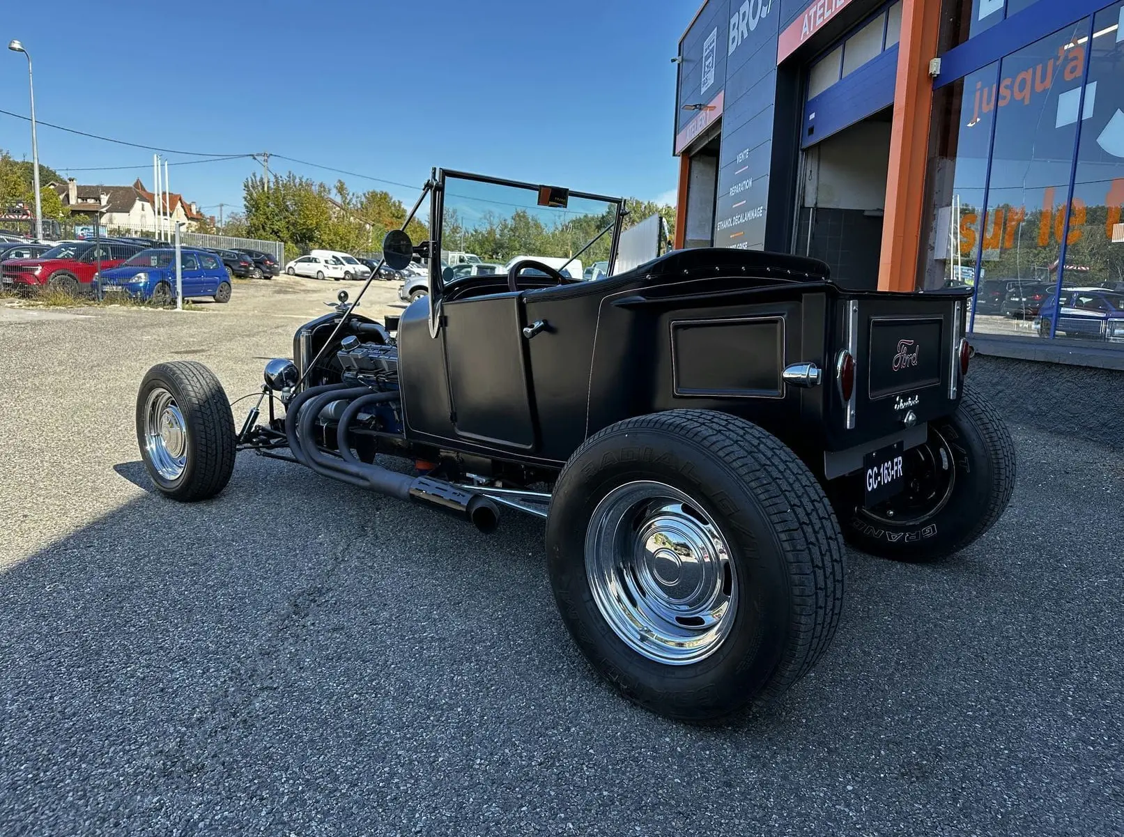 Ford T Hot Rod V8 noir vue 3/4 arrière droit, capote manuelle baissée et échappement latéral chromé visible