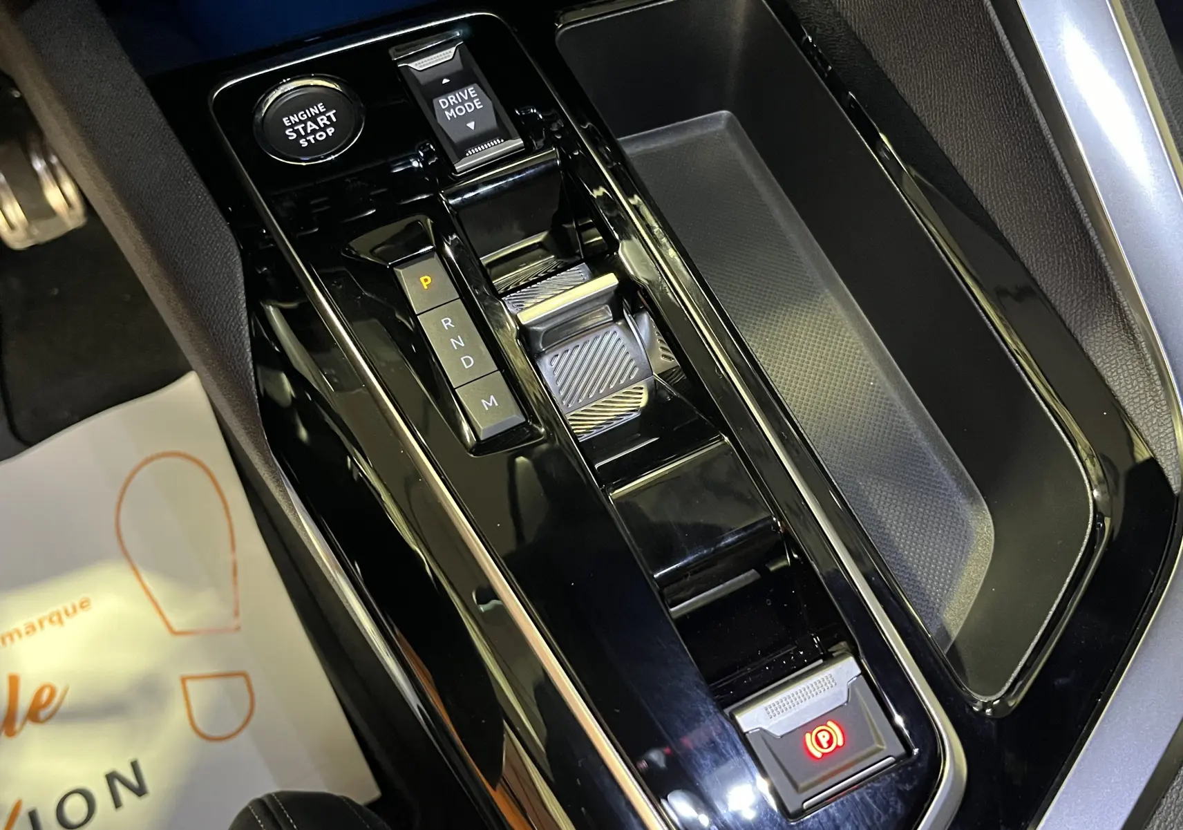 Vue rapprochée de la console centrale noire brillante du Peugeot 5008 2024, avec levier de vitesse automatique et bouton start-stop.