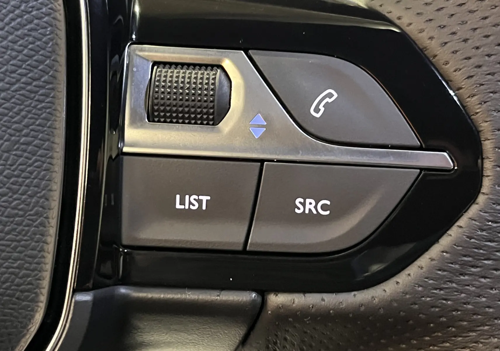 Gros plan sur les commandes de volume et assistant vocal sur le volant perforé du Peugeot 5008 gris platinium 2024.