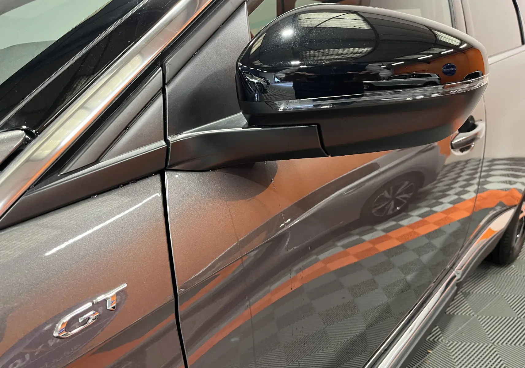Détail du rétroviseur noir brillant et de l’inscription GT sur la porte côté gauche d’un Peugeot 5008 gris platinium.