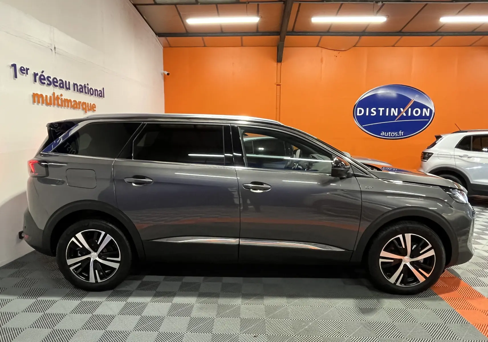 Profil droit d'un Peugeot 5008 gris platinium 2024 dans un showroom avec jantes bi-ton et vitres teintées.
