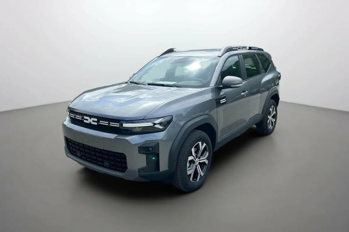 SUV Dacia Bigster gris schiste vu en 3/4 avant droit avec barres de toit et jantes alu 17 pouces.