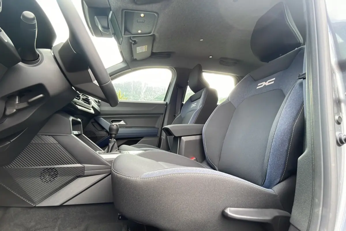 Vue intérieure côté conducteur du Dacia Bigster 2025, sièges noirs et gris avec logo DC brodé sur appuie-tête.
