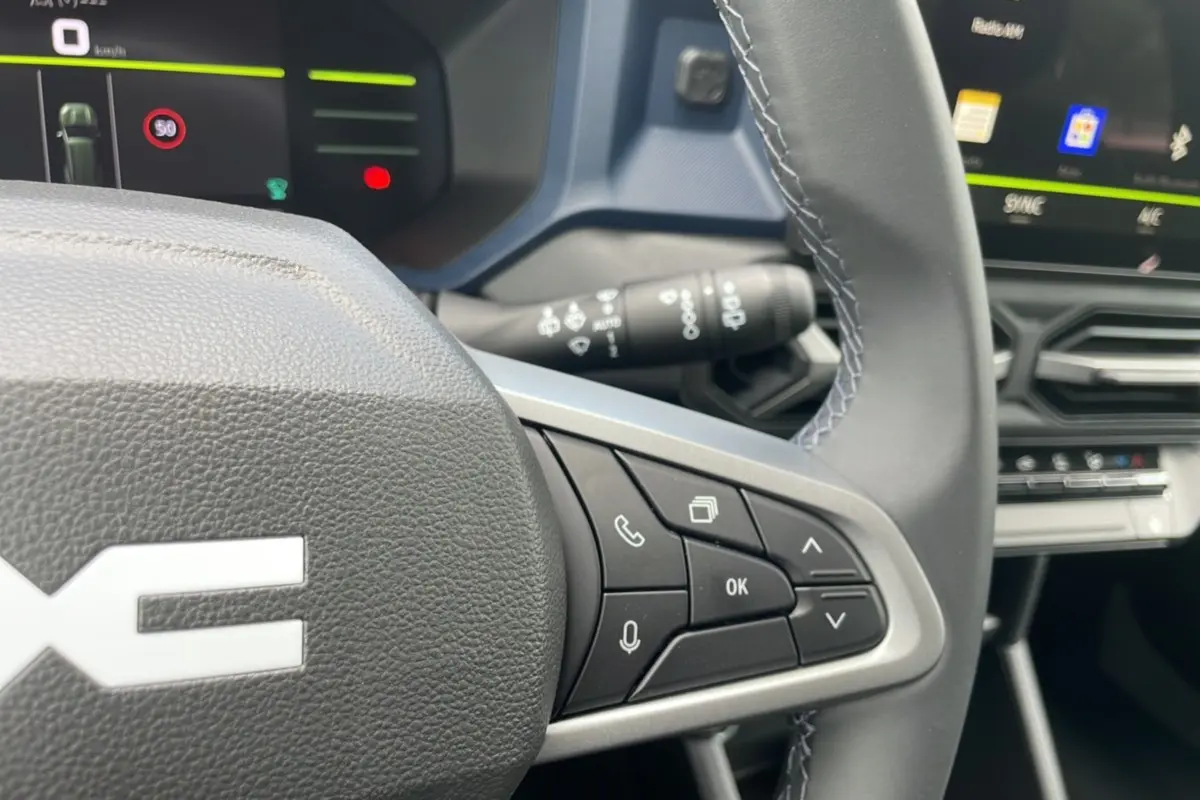 Gros plan sur le volant cuir gris du Dacia Bigster 2025 avec commandes multifonctions et tableau de bord numérique.