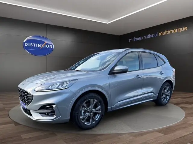 Vue 3/4 avant droite d'un Ford Kuga gris 2024 hybride essence, finition ST-LINE X avec jantes foncées et calandre distinctive.