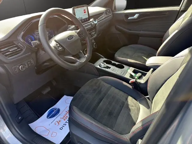 Vue intérieure côté conducteur du Ford Kuga 2024 gris, avec volant multifonction, écran tactile et sièges en tissu noir.