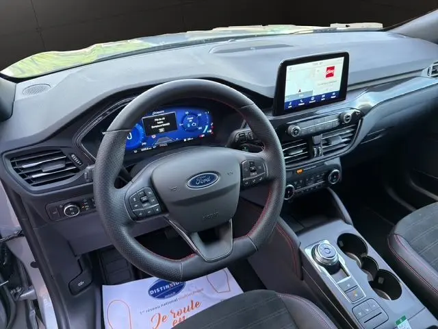 Vue intérieure du tableau de bord et volant du Ford Kuga gris 2024, avec écran tactile central et commandes au volant.