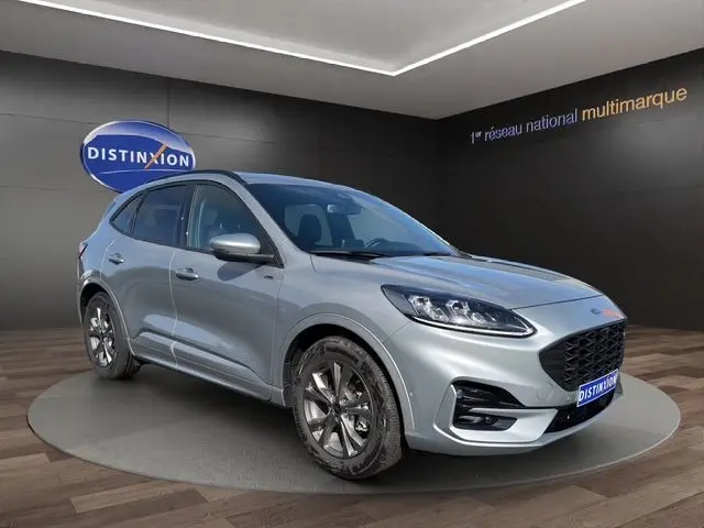 Vue 3/4 avant d'un Ford Kuga gris 2024 avec calandre noire et jantes foncées dans un showroom.