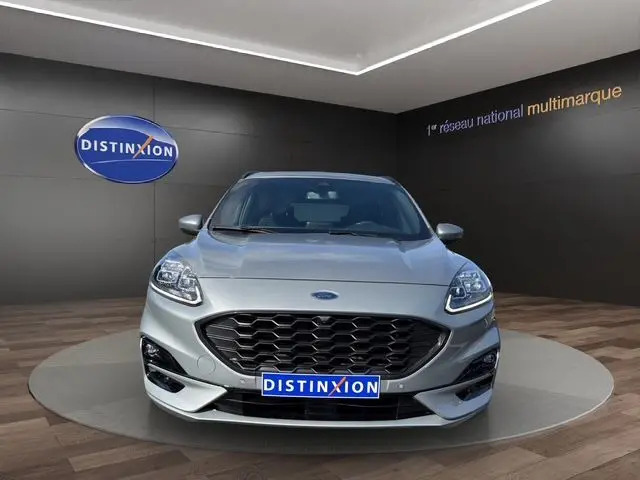 Vue de face d'un Ford Kuga gris 2024, version hybride ST-Line X avec calandre noire distinctive en showroom.