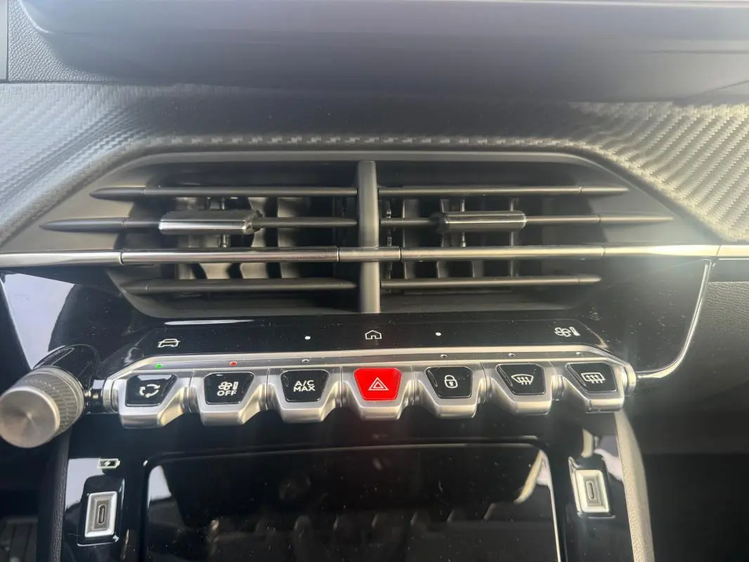 Détail du tableau de bord de la Peugeot 208 gris, montrant les commandes centrales et les aérateurs au-dessus.
