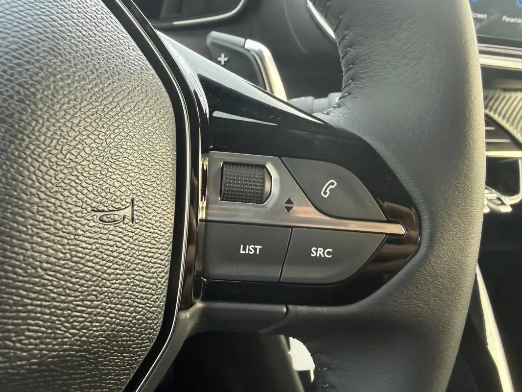 Gros plan sur les commandes gauche du volant noir du Peugeot 208 Hybrid 110 e-DCS6 Allure gris, avec boutons multifonctions.