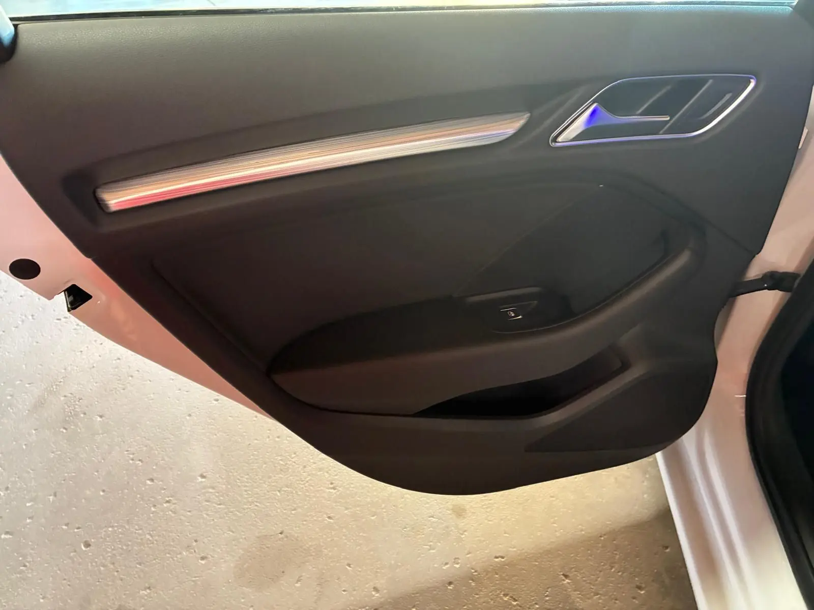 Vue intérieure de la porte côté gauche d'une Audi A3 Sportback blanche, avec garniture noire et insert décoratif argenté.